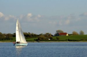 A sailboat is sailing on the water near some houses.