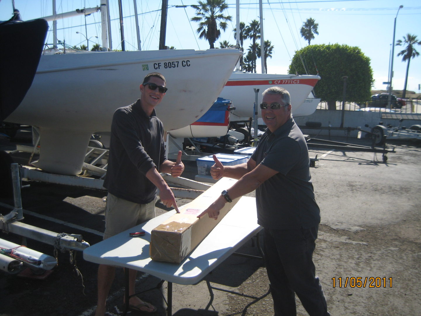 Two men cutting a piece of wood on top of a table.