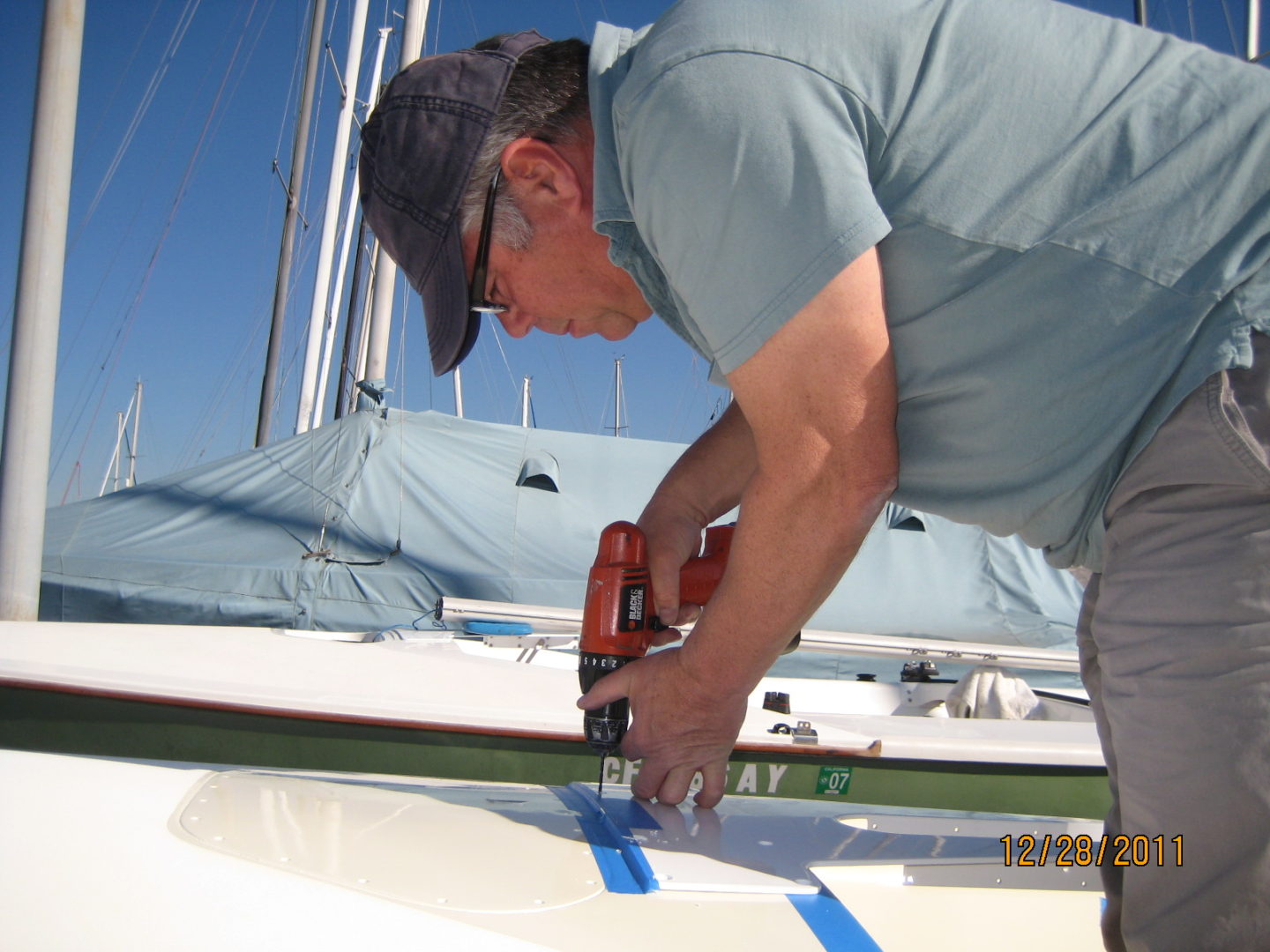 A man using a power drill on the side of a boat.