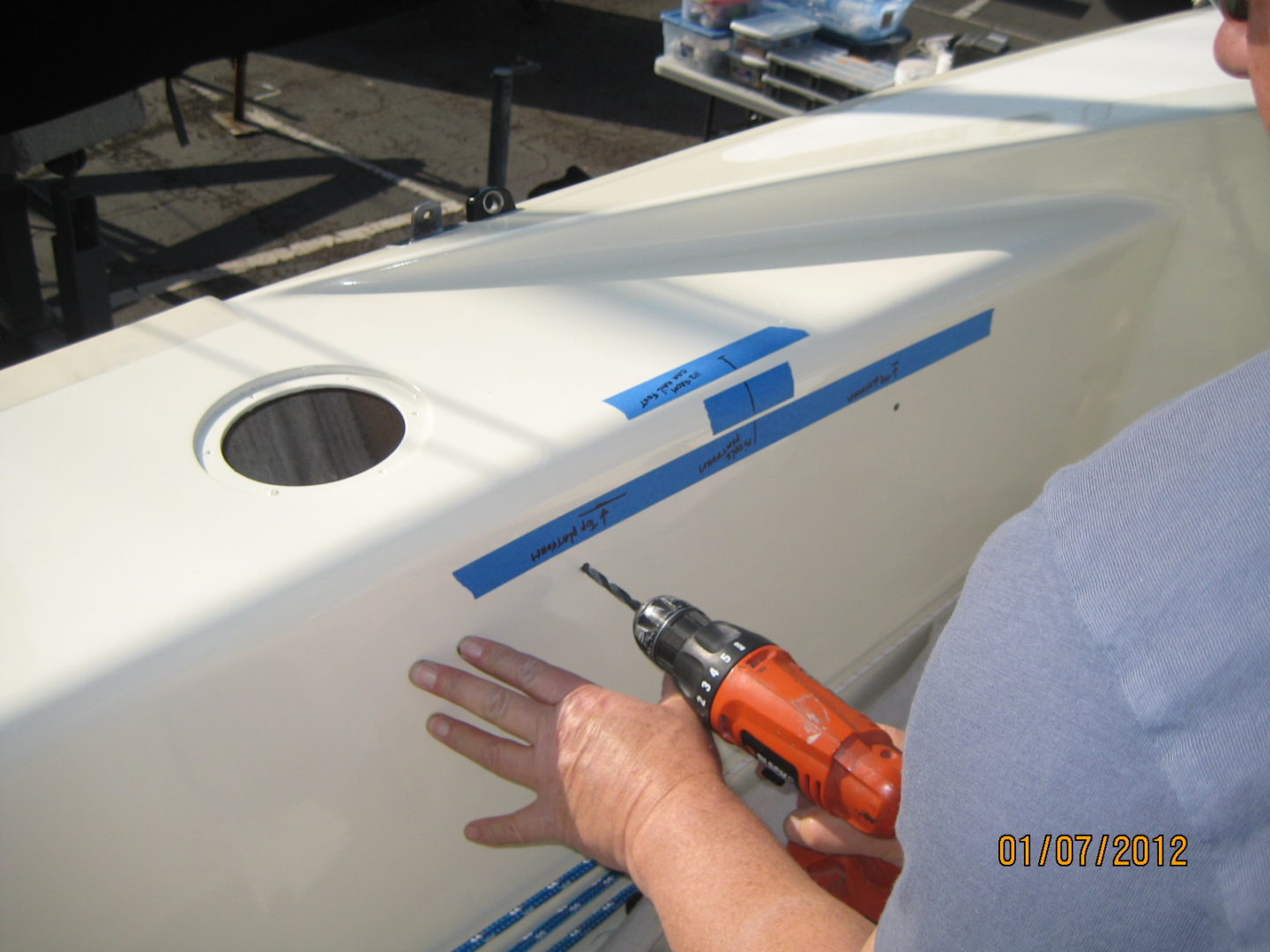 A person using an electric drill to fix the side of a boat.