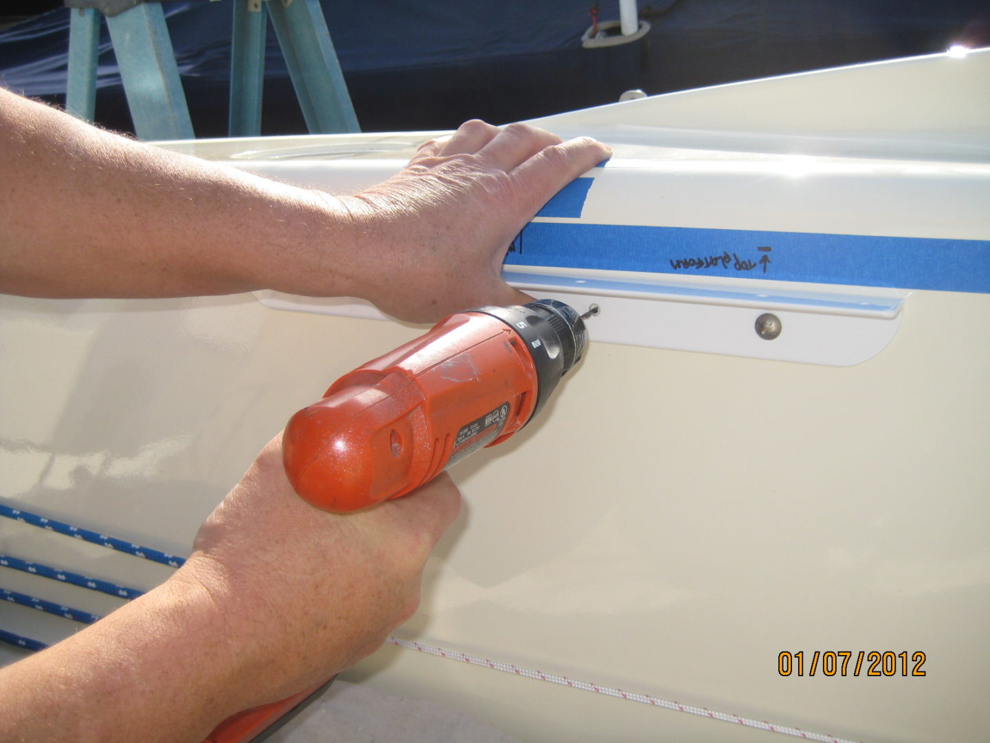 A person using an orange drill to fix the side of a boat.