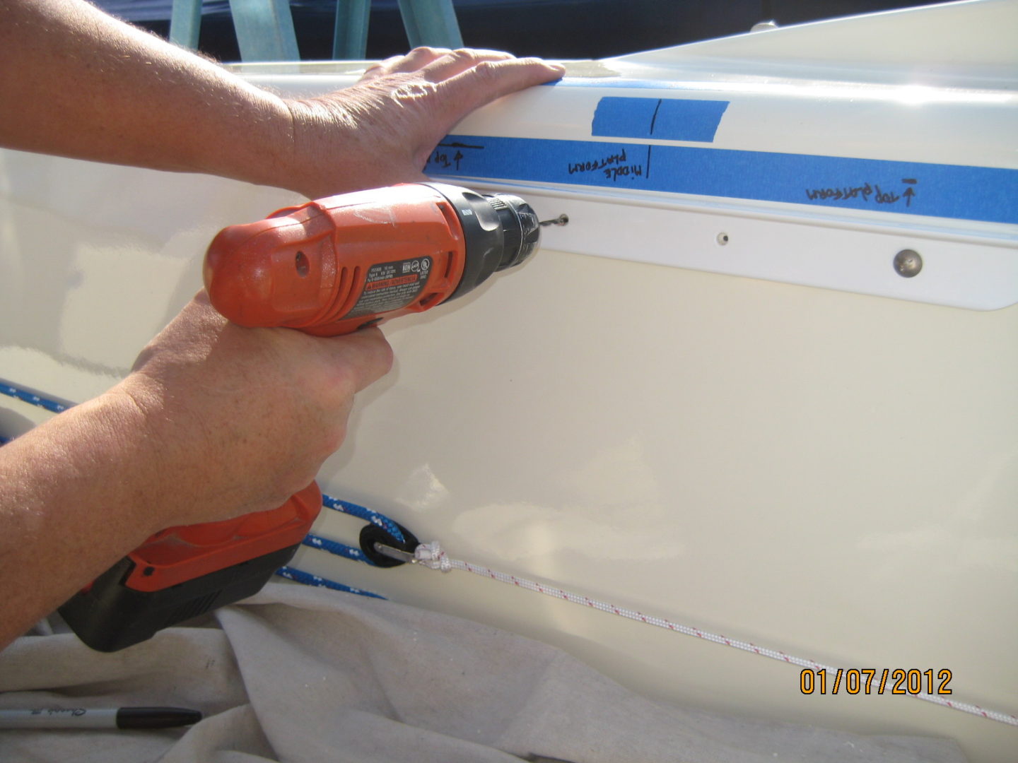 A person using an electric drill to install the side of a boat.