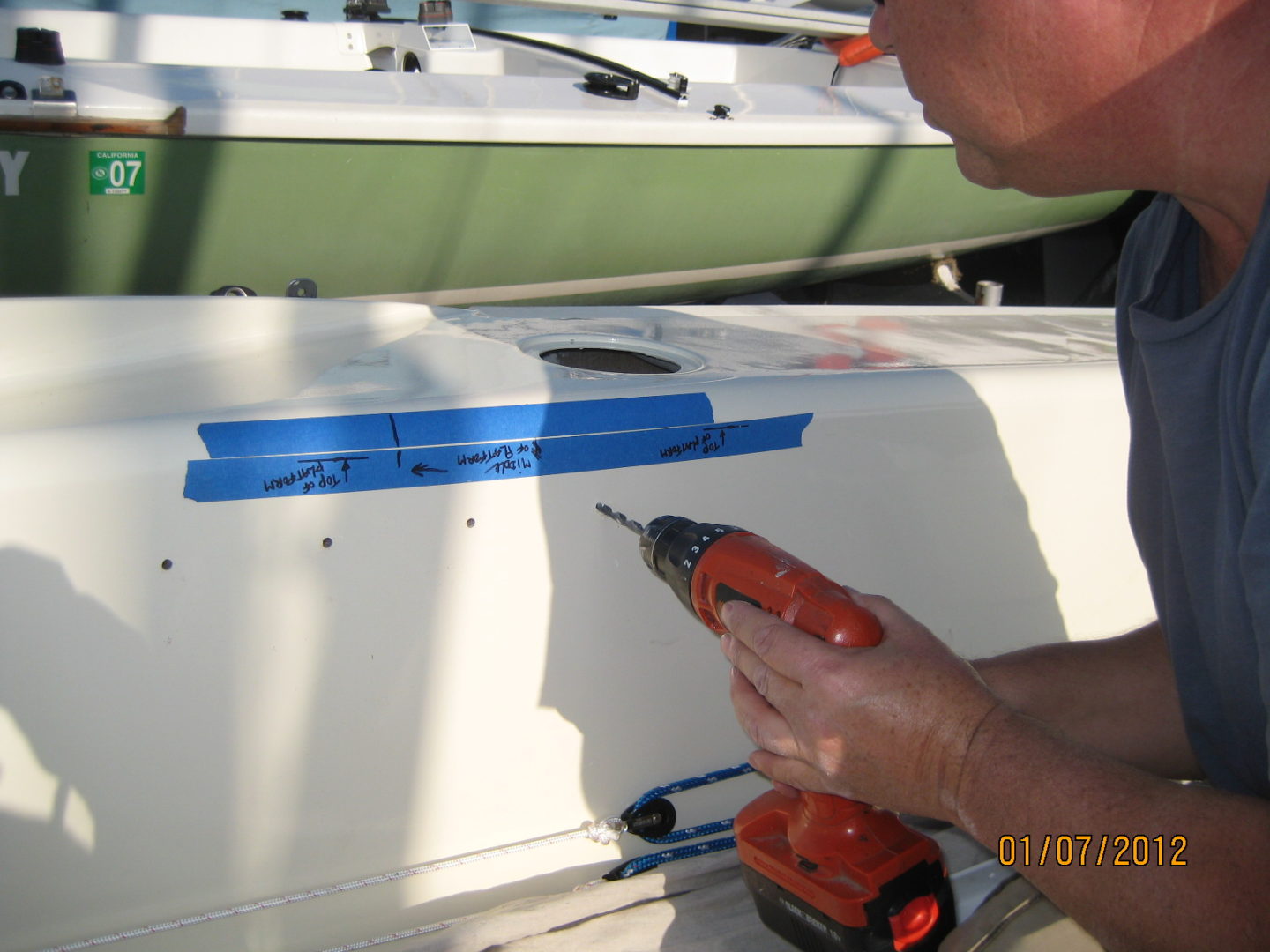 A man using an orange drill to install the side of a boat.