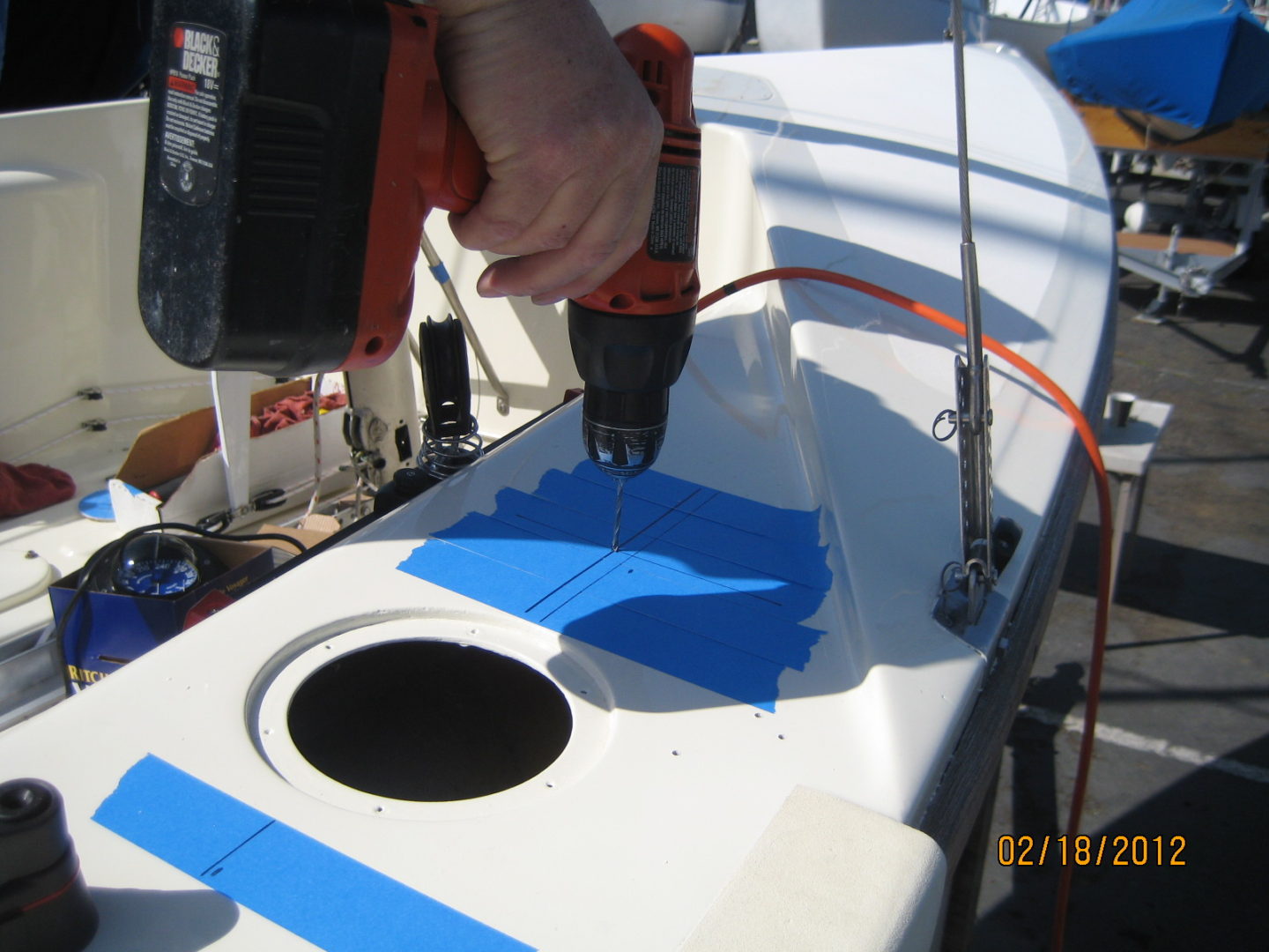 A person using an electric drill to install the blue tape on the side of a boat.