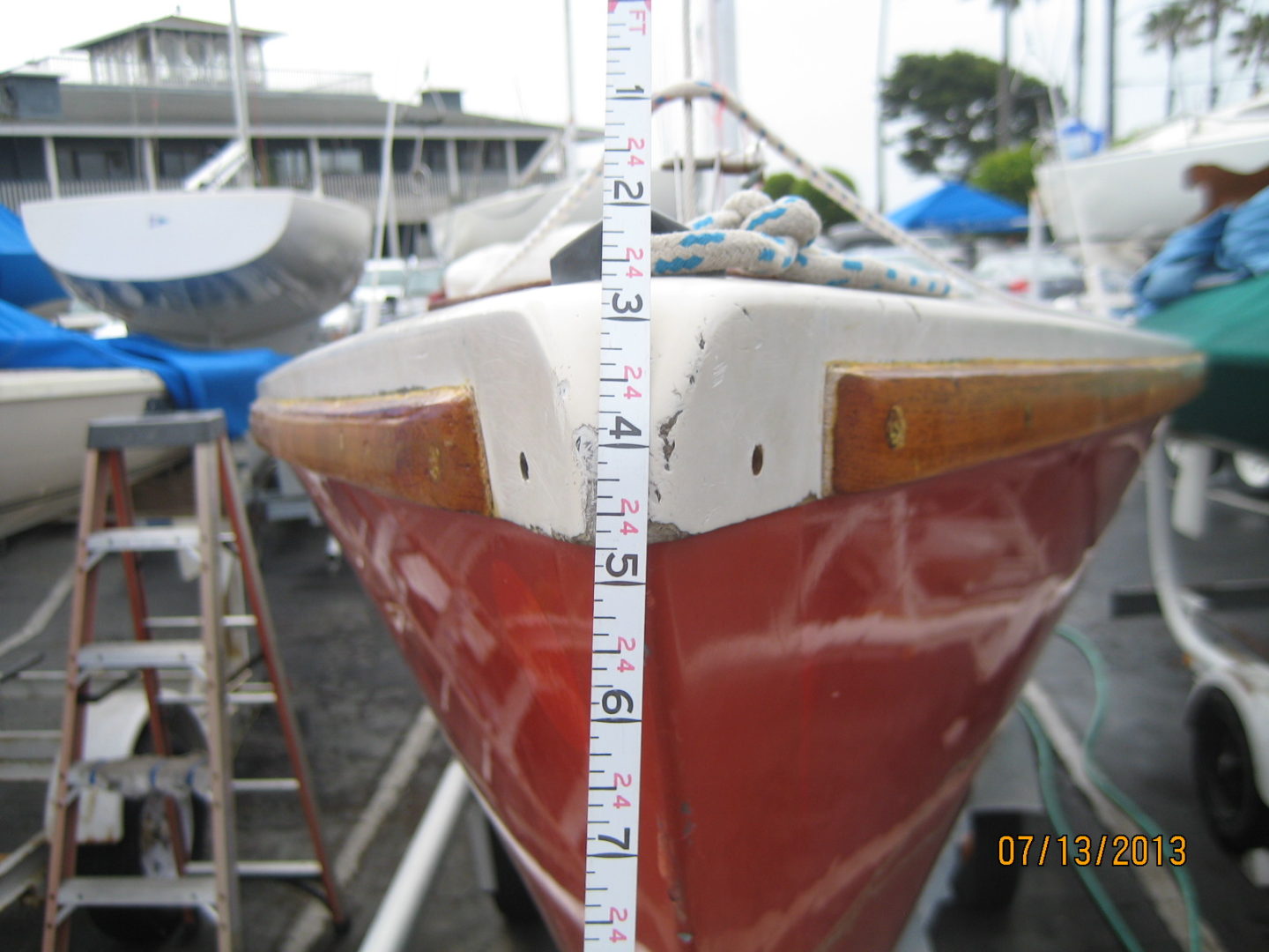 A red boat is in the water and has a white sail.