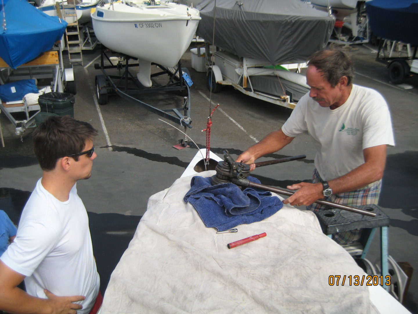 A man is helping another man to put up his sail.