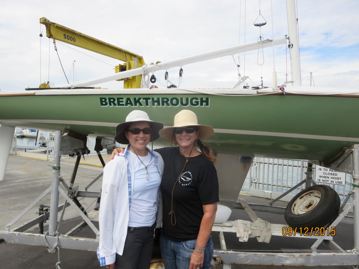 Two women standing next to a boat in front of the word breakthrough.