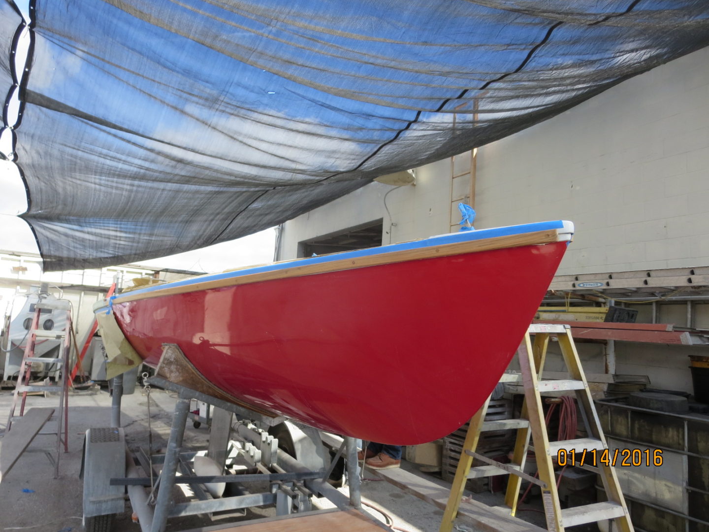 A red boat is being painted in the sun.