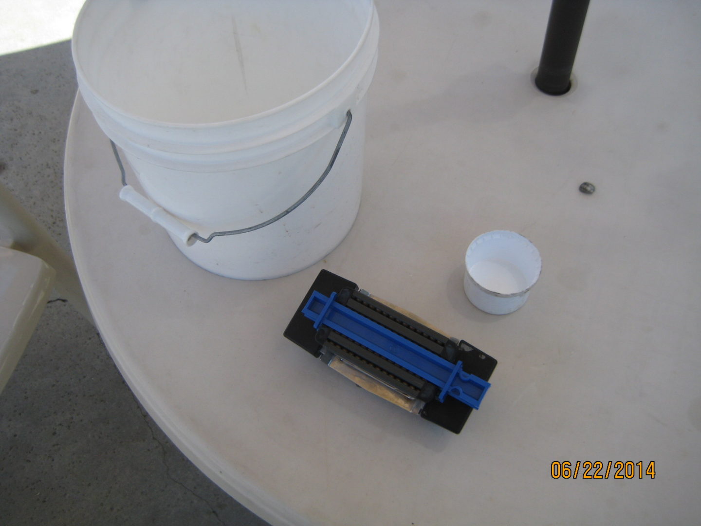 A white bucket and some blue plastic cups on top of a table.