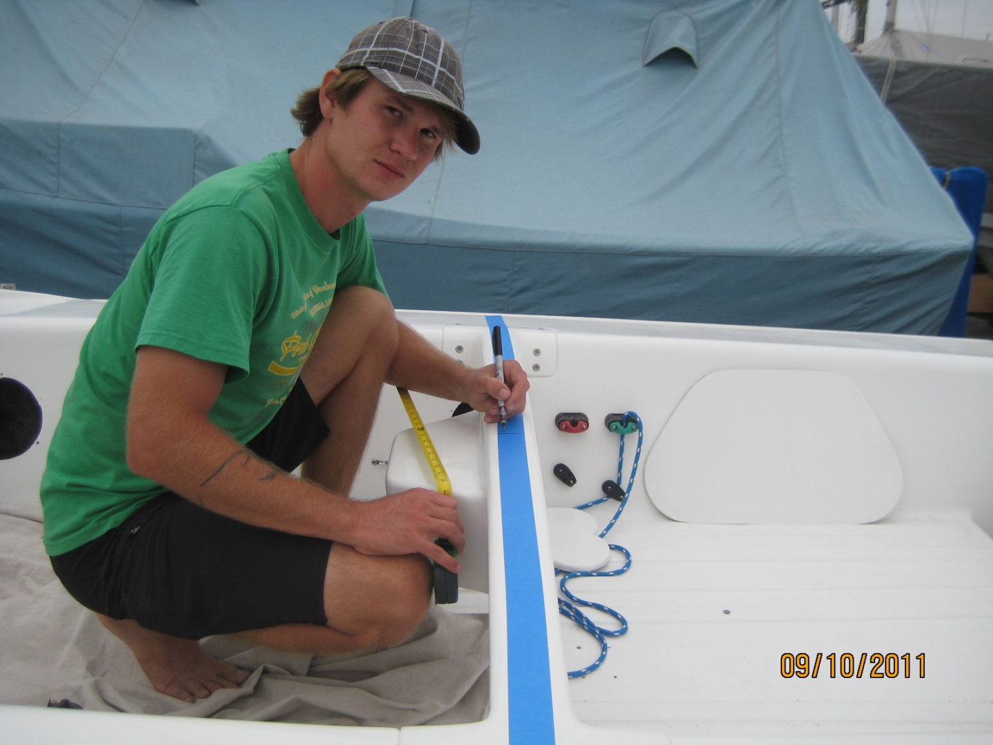 A man in green shirt painting blue lines on boat.